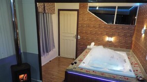 A room with a wood-burning stove, a hot tub with rose petals, and a stone wall. - Cabanas Costaneira  (Cambará do Sul)