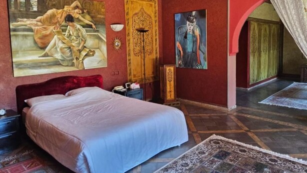 Une chambre à coucher avec un grand lit, une armoire en bois, un tableau accroché au mur et un tapis à motifs sur le sol.