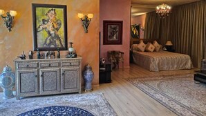 Une chambre d’hôtel avec un lit, un grand tableau, une commode ornée d’objets décoratifs et un lustre.