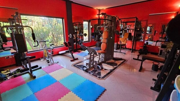 A gym with red walls, various exercise equipment, and a colorful floor mat. - Palais Oussoud Palmeraie (Marrakech)