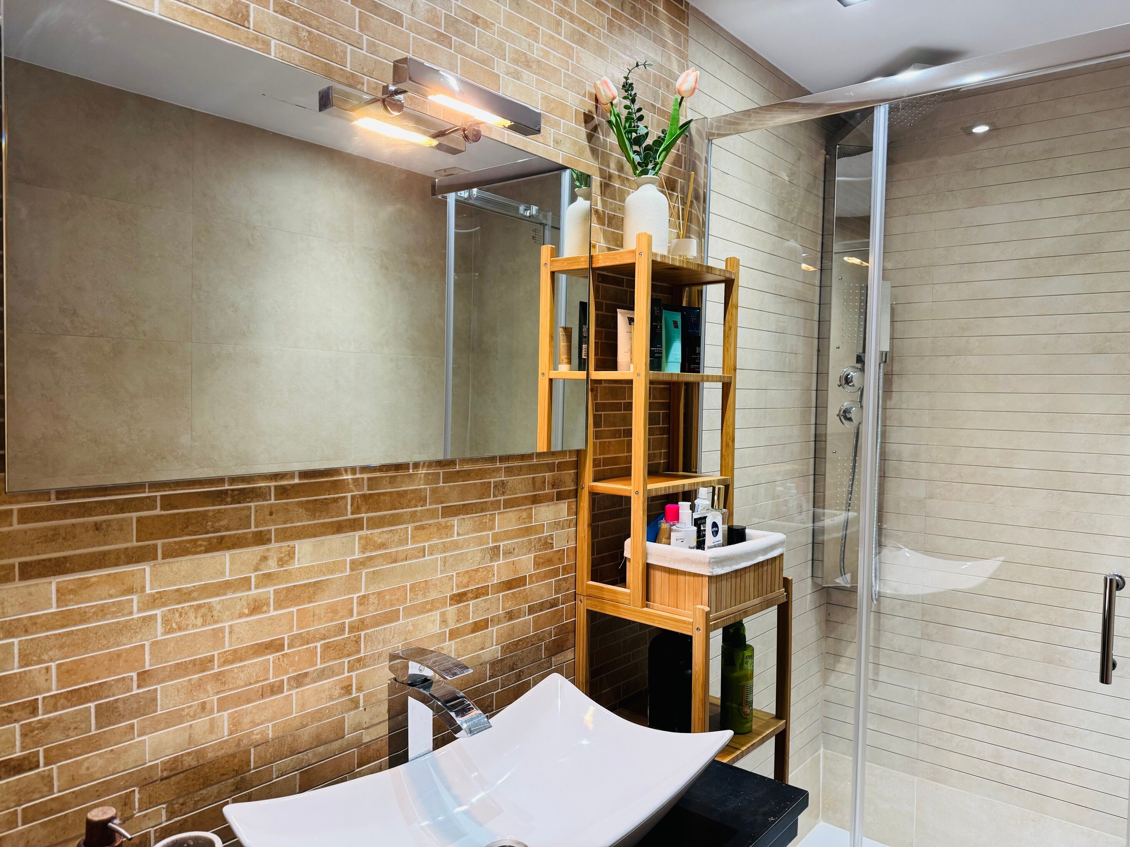 A bathroom with a white sink, a wooden shelf with toiletries, a mirror, and a shower area.