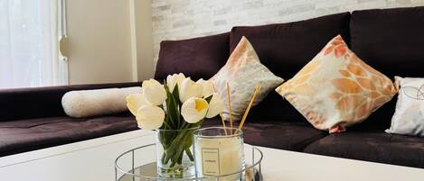 A modern living room with a white coffee table, a glass candle holder with white flowers, and a tray with chocolates.