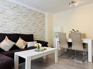 A modern living room with a dark brown sofa, white coffee table, and a dining area with a white table and two chairs. - Apartment 'Comodidad Cerca Del Centro Granada' with Shared Pool, Wi-Fi and Air Conditioning (Albolote)