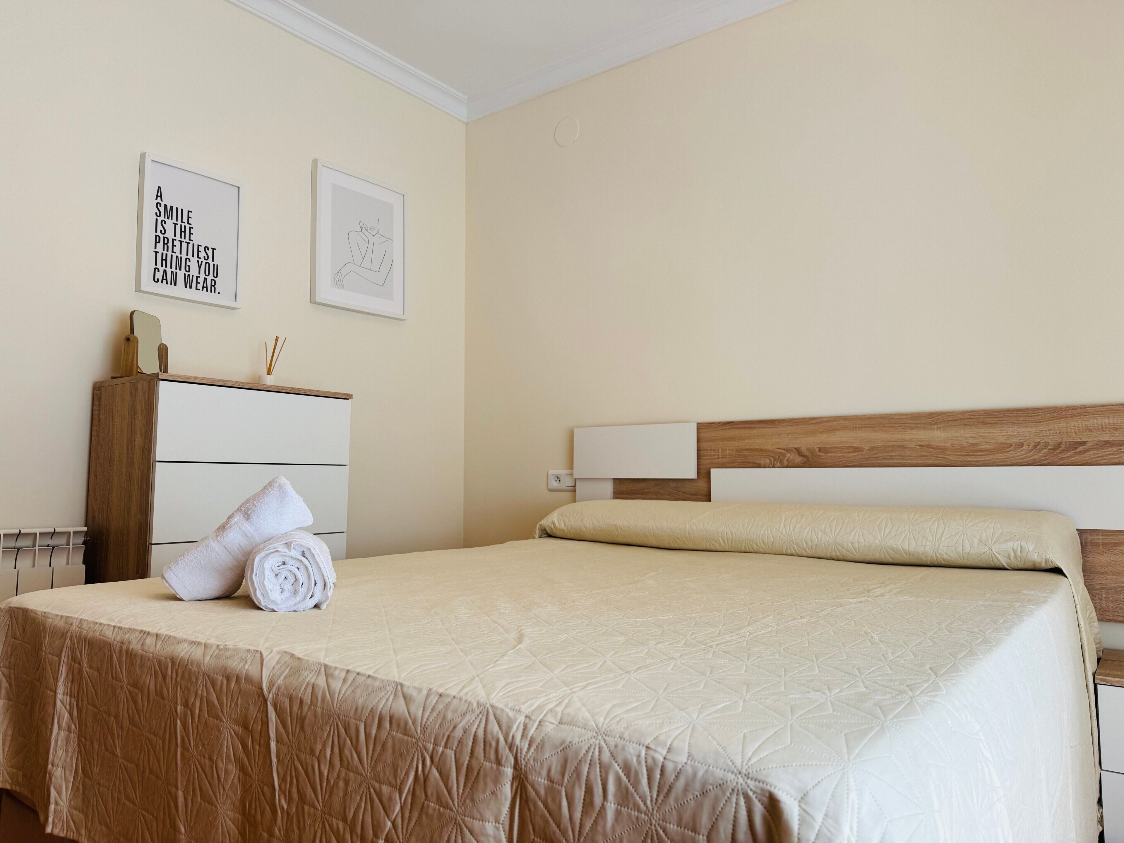 A neatly made bed with a quilted cover, a wooden headboard, and a bedside table with a mirror and a small decorative item.
