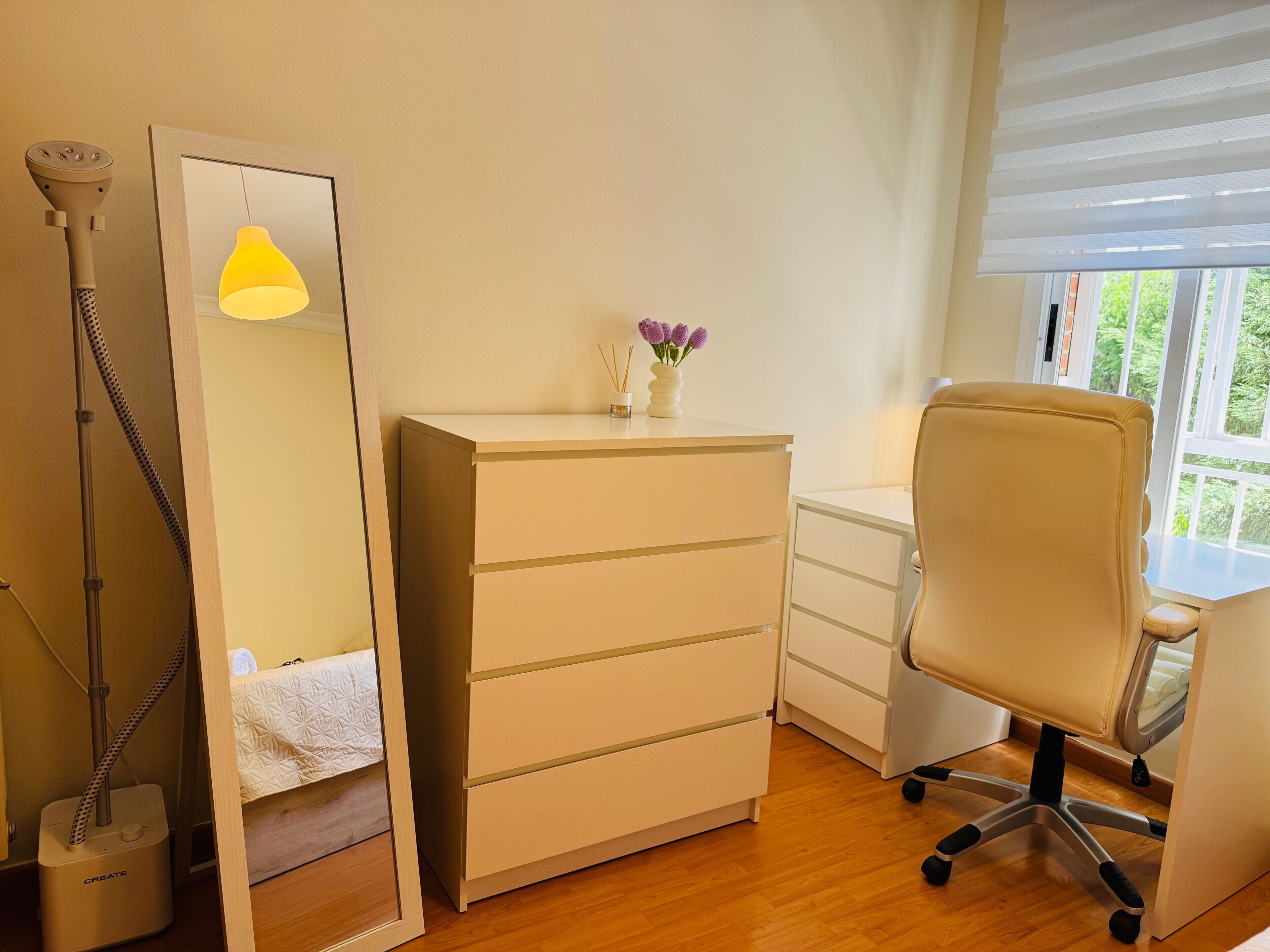 A room with a desk, chair, mirror, and a standing lamp.