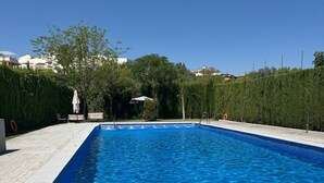 Una piscina rectangular con agua cristalina azul, rodeada por un patio empedrado y un seto.