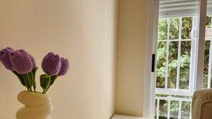 Un florero blanco con diseño texturizado sobre una mesa blanca, cerca de una ventana con vistas a la vegetación.