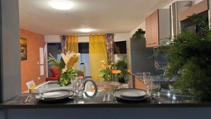 Een moderne keuken met een eetgedeelte, met een tafel met glazen blad, keukenapparatuur en decoratieve planten.