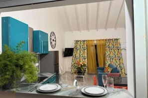 Un espace de vie compact comprenant un coin cuisine, une table à manger pour deux personnes et un salon avec un canapé et des rideaux.