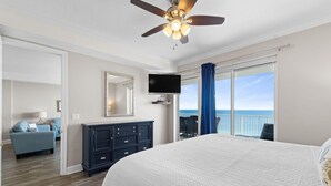Una camera da letto con un letto grande, una ventola a soffitto, una televisione, un comò e vista sull'oceano tramite una porta scorrevole.