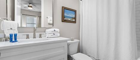 Un baño con un tocador blanco, un inodoro, una cortina de ducha y un cuadro en la pared.