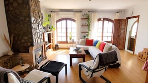 A living room with a fireplace, a sofa with colorful cushions, a coffee table, and a chair. - Holiday Home 'Monte Azul' with Private Pool, Wi-Fi and Air Conditioning (Benajarafe)