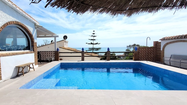 A swimming pool with a view of the sea, a covered patio, and a building with a tiled roof. - Holiday Home 'Monte Azul' with Private Pool, Wi-Fi and Air Conditioning (Benajarafe)
