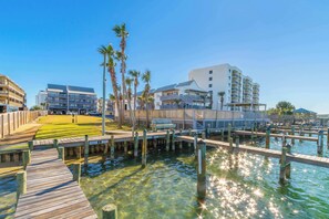 A waterfront property with a wooden dock, clear water, and modern buildings in the background. - 1 bed Beach, Pools, Waterfront, Boating | Palmaway (Orange Beach)