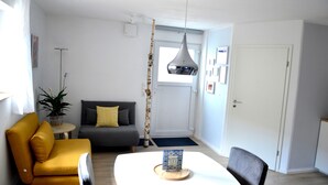 Ein modernes Wohnzimmer mit einem gelben Sofa, einem grauen Schlafsofa, einem weißen Tisch mit einem dekorativen Gegenstand und einer Pendelleuchte.