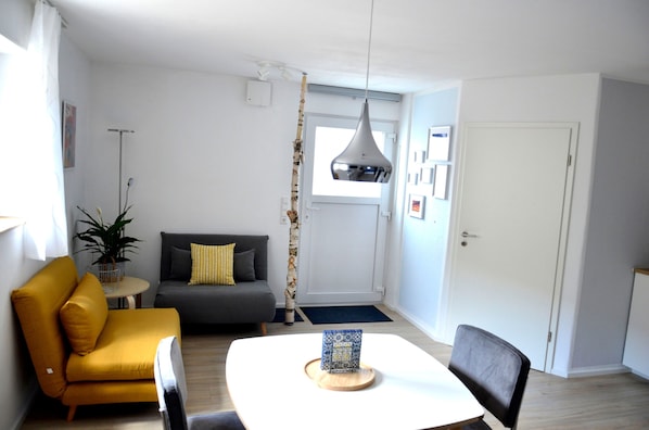 A modern living room with a yellow sofa, a grey couch, a white table with a decorative item, and a hanging light fixture.