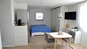 Ein Schlafzimmer mit Bett, Schreibtisch mit Stuhl, Fernseher und Fenster.