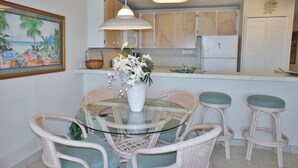 Una cocina con una mesa de vidrio y sillas de mimbre, una lámpara colgante y un refrigerador.