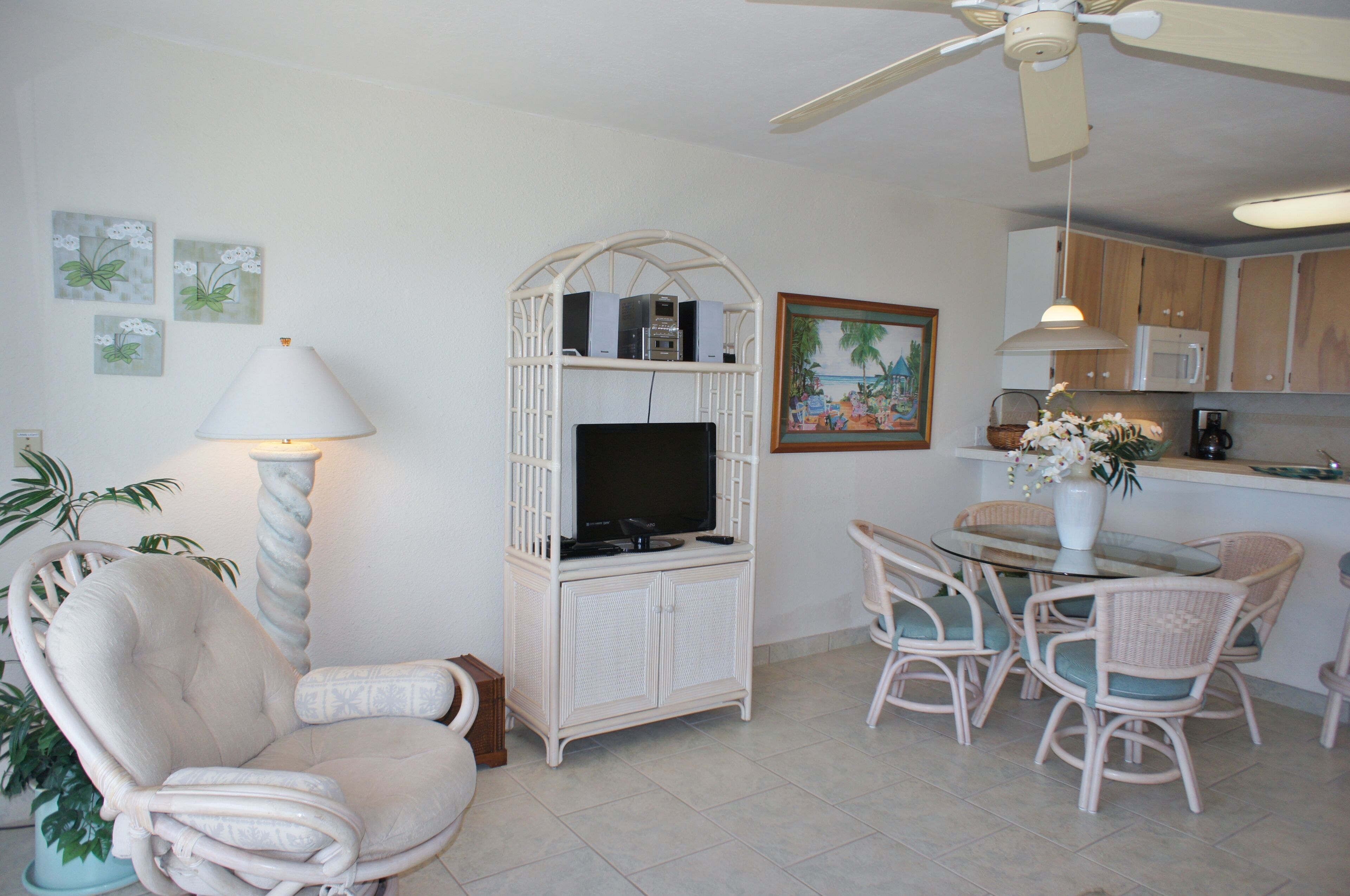 Un salon comprenant un téléviseur, une table à manger avec des chaises, un ventilateur de plafond et une étagère murale avec des haut-parleurs.