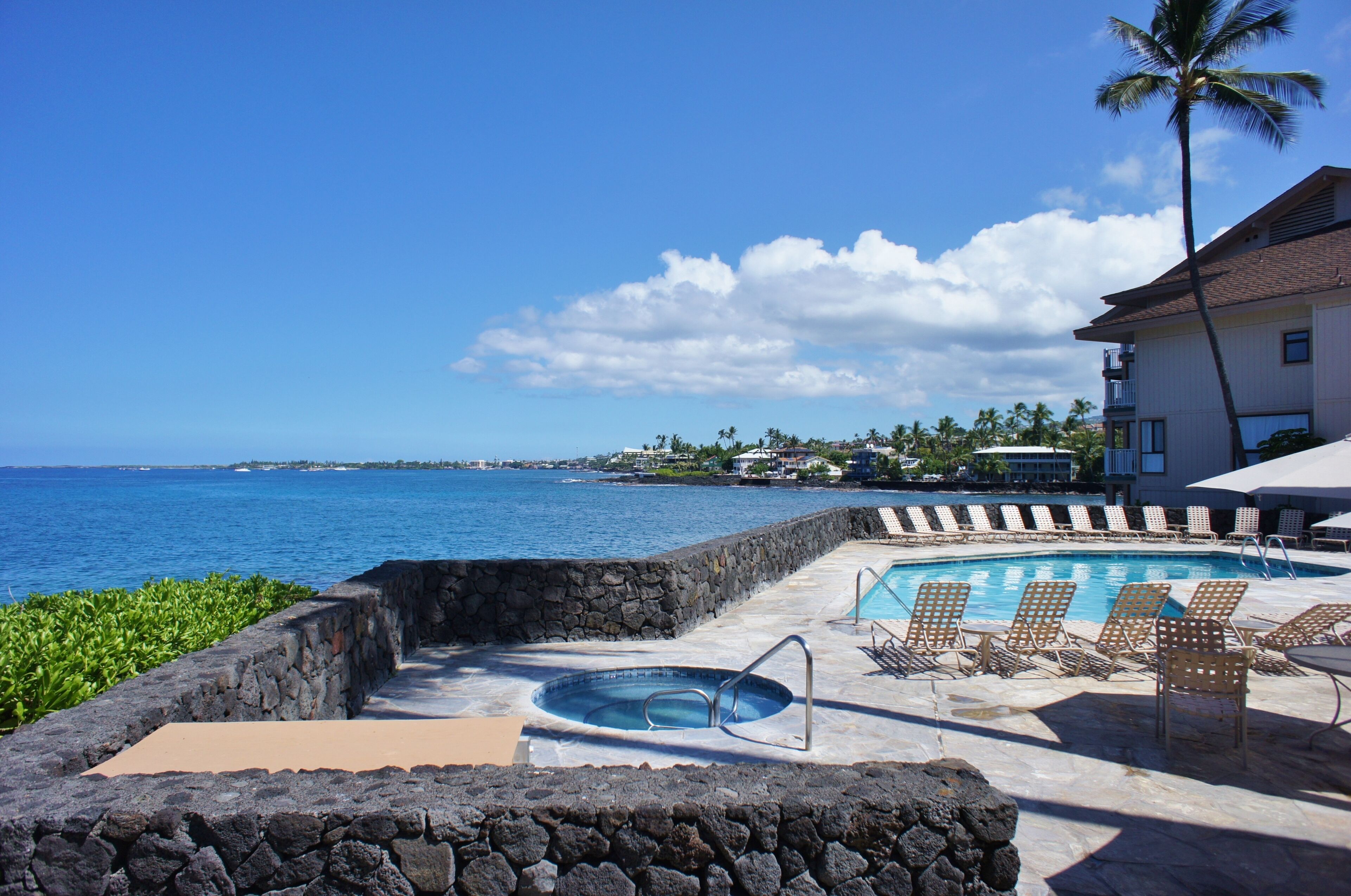 A pool area with lounge chairs, a hot tub, and a view of the ocean.
