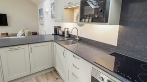 A modern kitchen with white cabinets, a black countertop, a microwave, a toaster, and a dishwasher. - Hideaway Cottage No 1 (Seahouses)