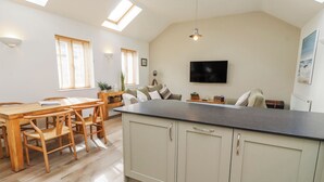 A spacious kitchen with a large island, wooden dining table, and chairs. - Hideaway Cottage No 1 (Seahouses)
