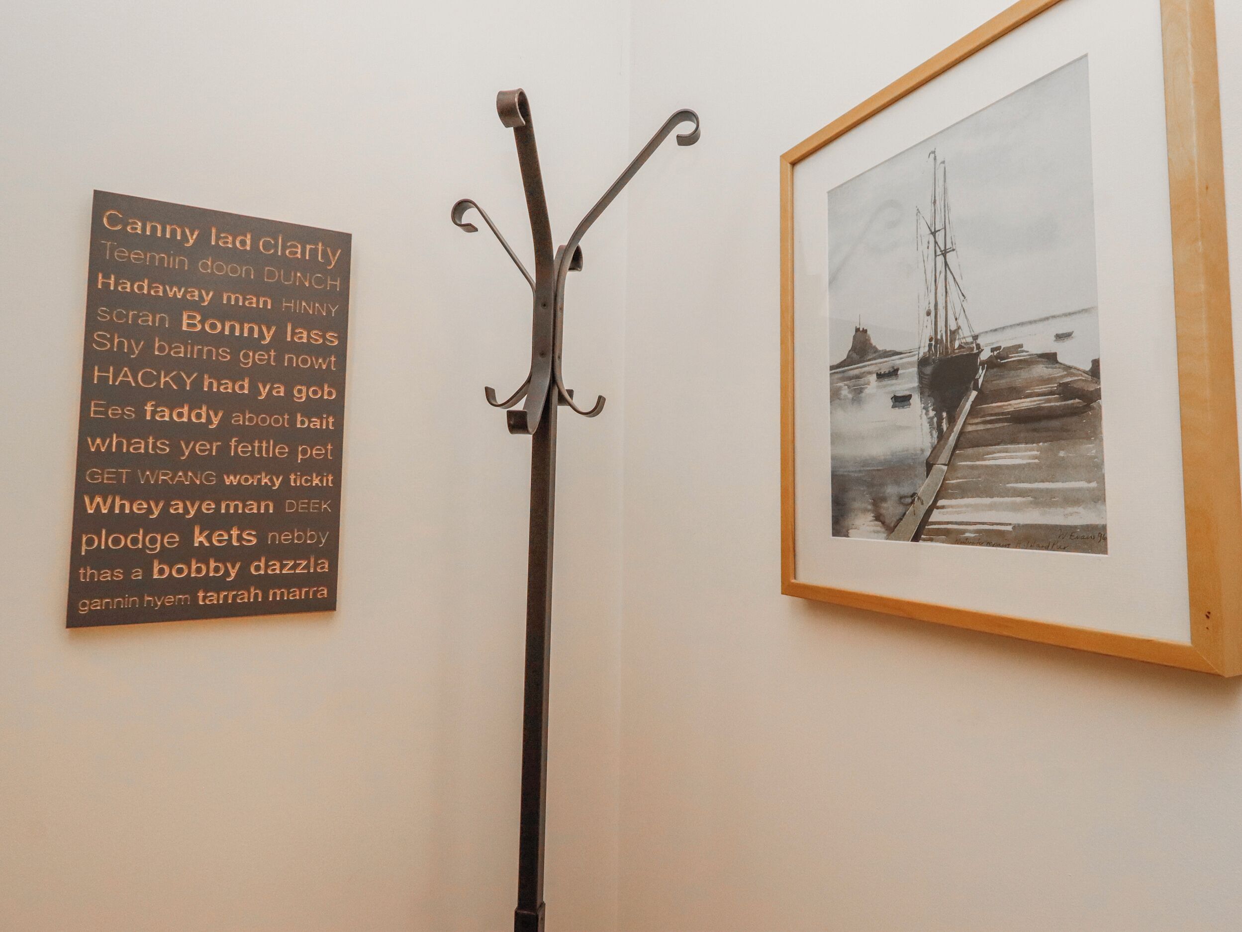 A wall with a metal coat rack and a framed picture of a ship.
