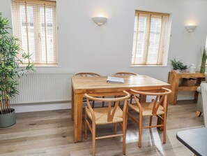 Ein Essbereich mit Holztisch und Stühlen, zwei Wandleuchten und Fenstern mit Jalousien.
