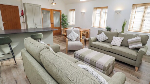 A modern living room with a sofa, ottoman, and a dining area with a table and chairs. - Hideaway Cottage No 1 (Seahouses)