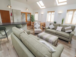 A modern living room with a sofa, ottoman, and a dining area with a table and chairs. - Hideaway Cottage No 1 (Seahouses)
