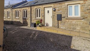 A stone building with multiple windows, a door, and a small garden area with plants. - Hideaway Cottage No 1 (Seahouses)