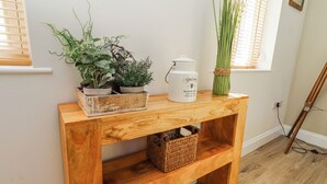 A wooden console table with potted plants, a white teapot, and a wicker basket. - Hideaway Cottage No 1 (Seahouses)