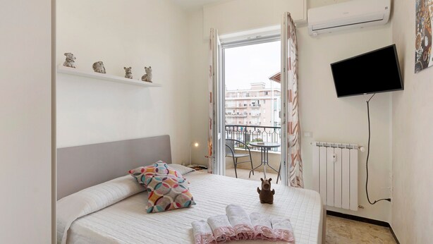 Ein Schlafzimmer mit Bett, Fernseher, Heizkörper und Balkonblick.