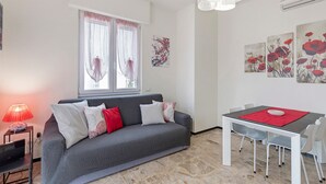 Ein modernes Wohnzimmer mit einem grauen Sofa, einem Esstisch mit Stühlen, einer roten Tischläufer und Bildern an den Wänden.