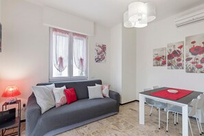 A modern living room with a grey sofa, a dining table with chairs, a red table runner, and artwork on the walls. - Apartment 'Alloggio Gallinara' with Sea View, Wi-Fi, and Air Conditioning (Albenga)