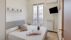 Ein Schlafzimmer mit einem Bett, einem Fernseher, einem Fenster mit Vorhängen und einer Heizung.