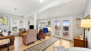 A spacious living room with a large window, a fireplace, and a view of the beach. - Amelia Island Beach Bungalow Directly on the Beach - Upstairs unit (Fernandina Beach)