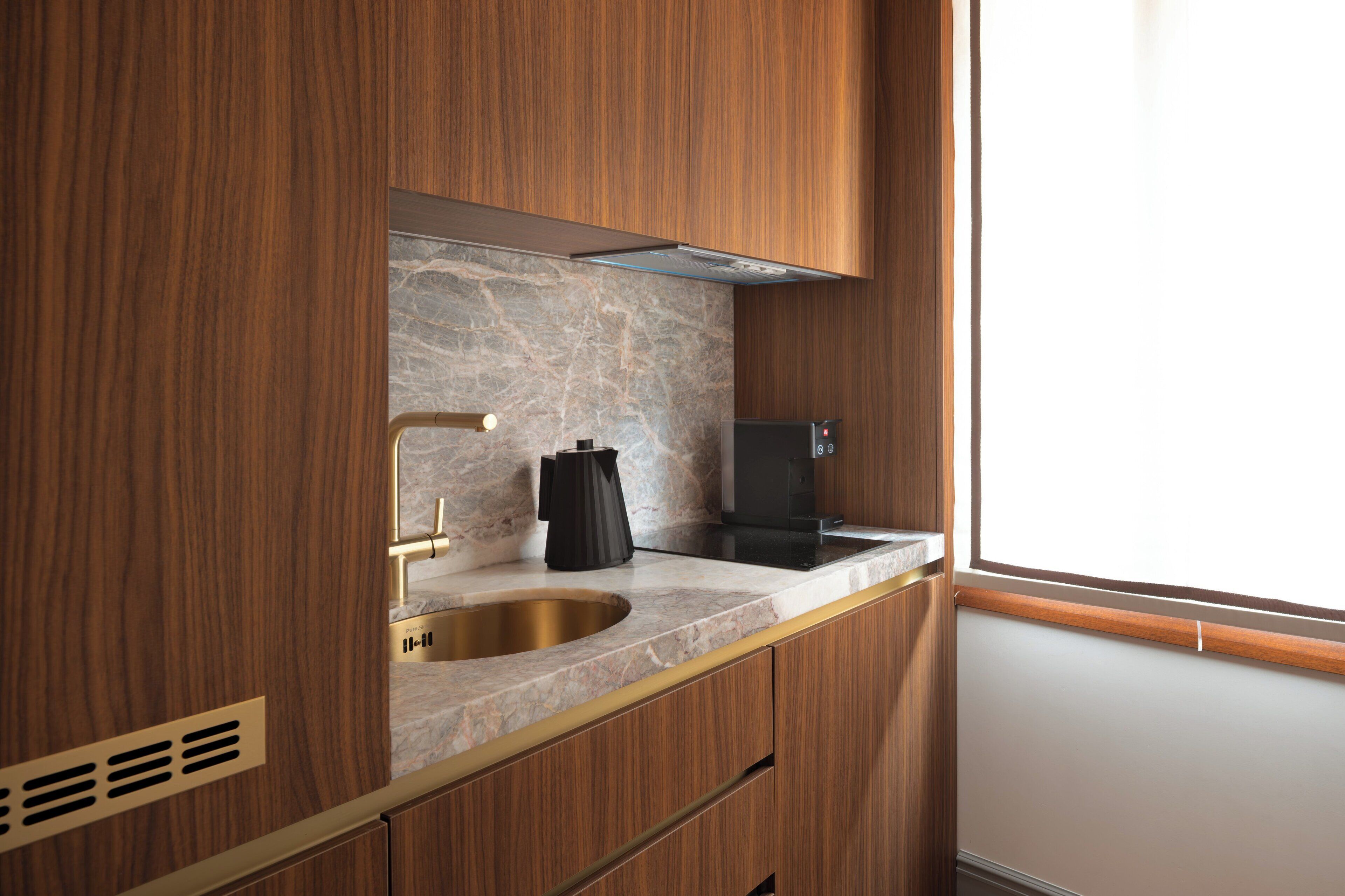 A modern kitchen with a marble countertop, a stainless steel sink, and wooden cabinetry.