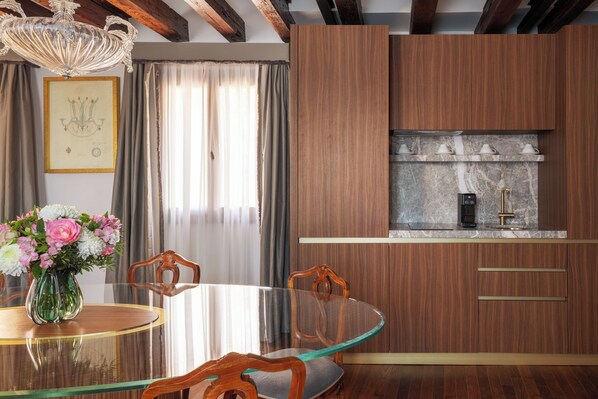 A dining area with a glass table, wooden chairs, a vase with flowers, and a kitchen with wooden cabinets and a marble countertop. - Gabrielli Luxury Apartments Venezia - Starhotels Collezione (Venice)