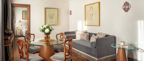 A living room with a glass coffee table, wooden chairs, a grey sofa, and framed artwork on the walls.