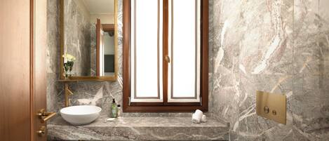 A bathroom with a marble sink, a large mirror, and a wooden-framed window.