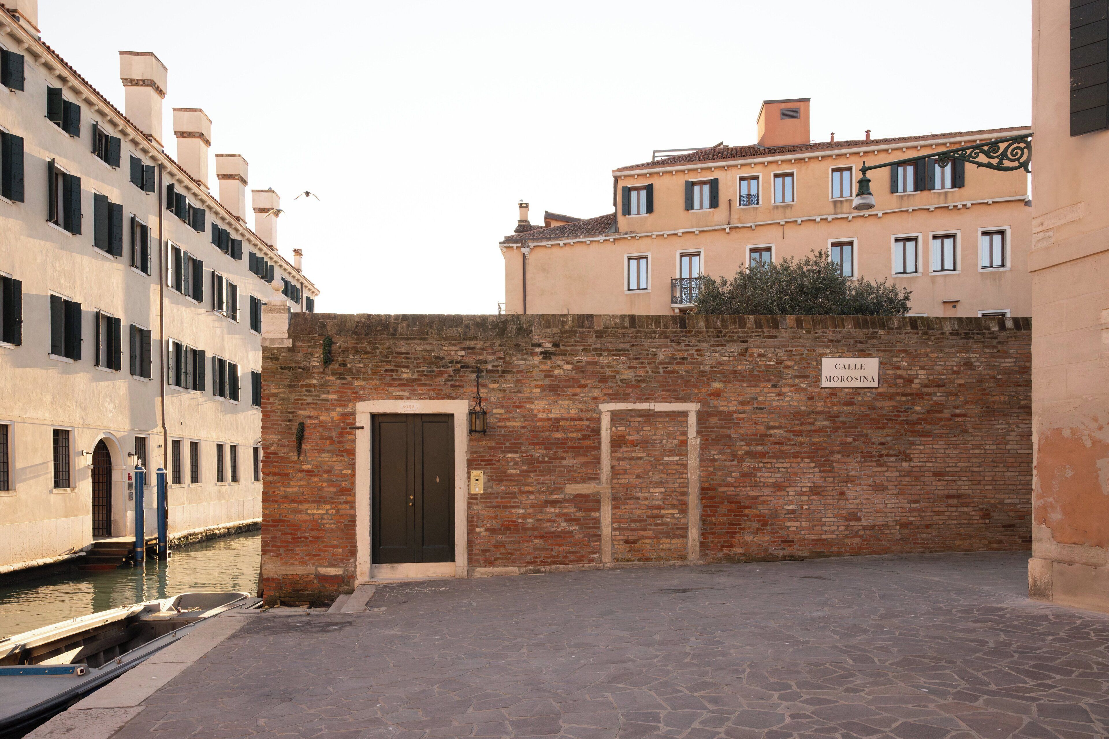 A narrow alley with a brick wall, a canal, and buildings with balconies.