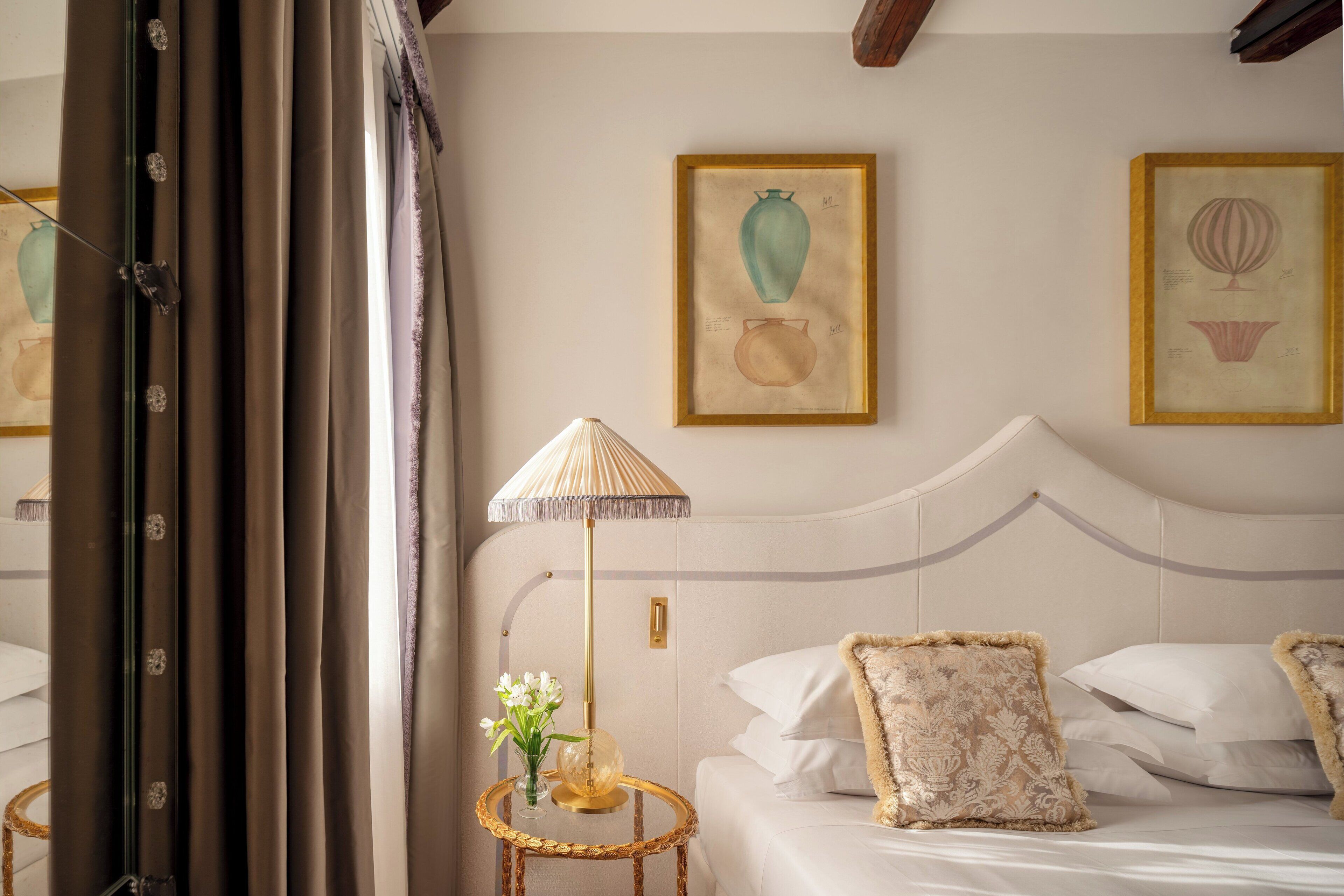 A neatly arranged bedroom with a bed, pillows, a bedside lamp, and framed artwork on the wall.
