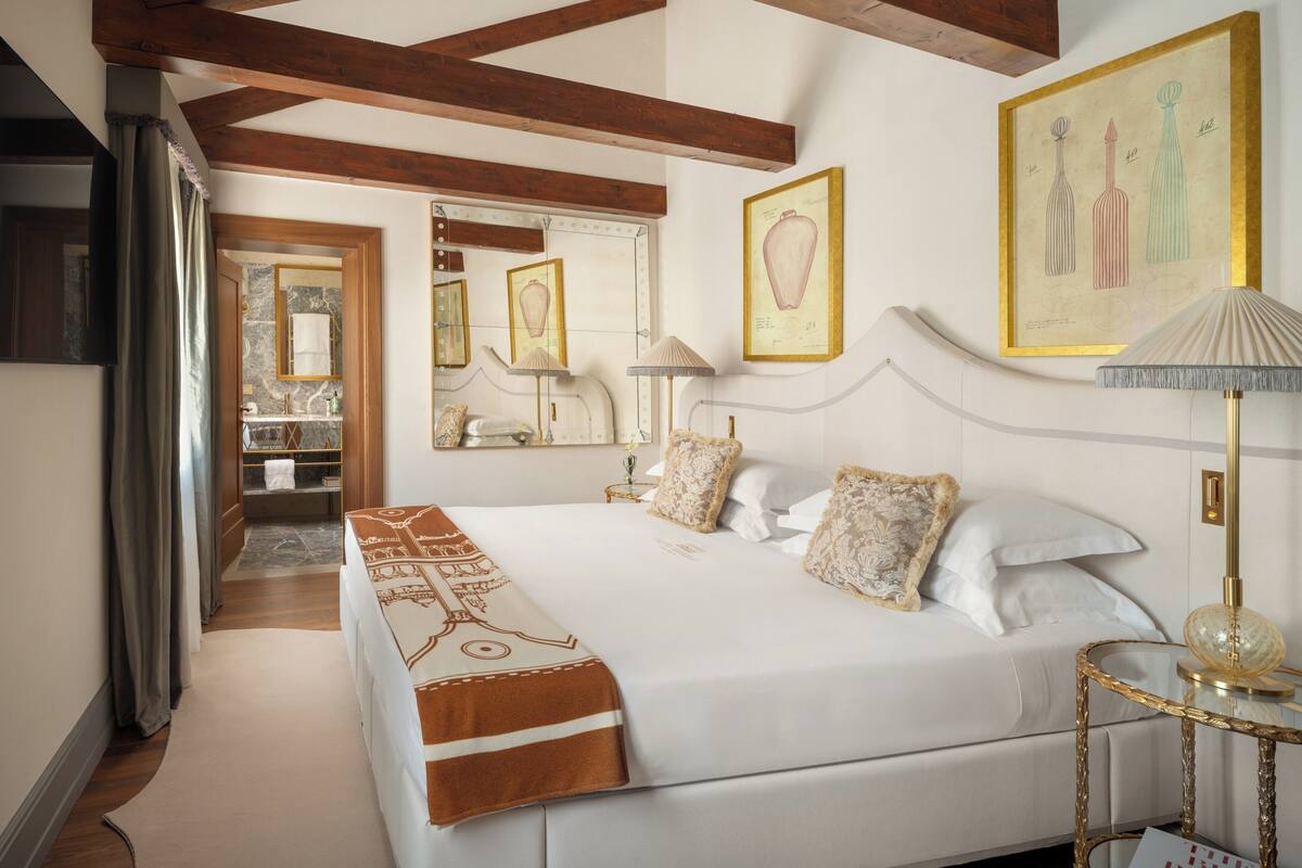 A bedroom with a large bed, a bedside table, a lamp, and a framed artwork on the wall.