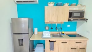 A compact kitchen with a stainless steel refrigerator, a microwave, a sink, and wooden cabinets. - Charming 1-bedroom apartment in perfect Oranjestad with outside Pool (Oranjestad)