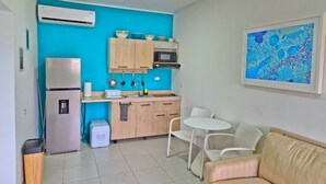 A compact kitchen with a refrigerator, microwave, and wooden cabinets. There is a dining area with a white table and chairs. - Charming 1-bedroom apartment in perfect Oranjestad with outside Pool (Oranjestad)