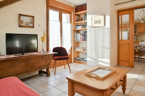 Un salon avec un téléviseur, un fauteuil rouge, une table basse en bois et une bibliothèque.