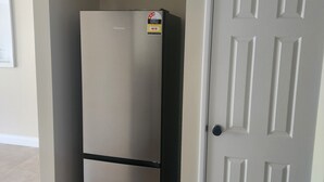 A compact, two-door refrigerator with a visible energy efficiency rating sticker, positioned next to a white door with a decorative panel design. - West Perth apartment. Walking distance to CBD, King's Park and Public transport. (West Perth)