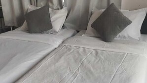 Een hotelkamer met twee bedden, elk met witte lakens en grijze kussens.