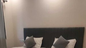 Een tweepersoonsbed met een donker hoofdbord, twee kussens en een witte sprei in een kamer met een betegelde vloer.